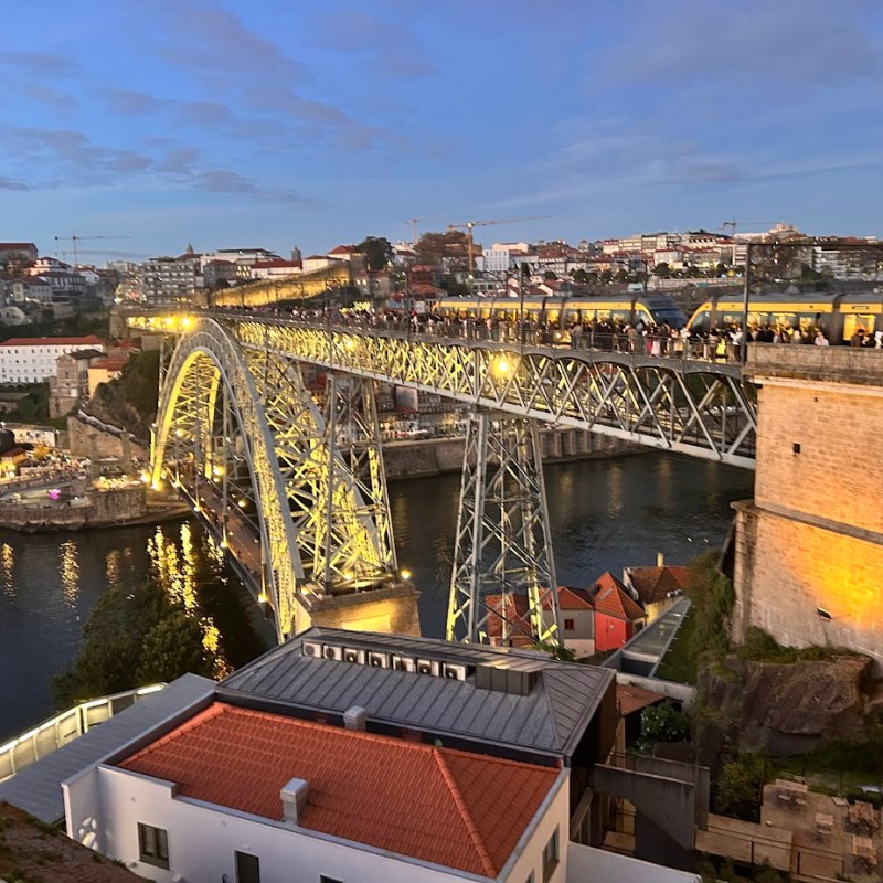 Illuminated bridge over river surrounded by cityscape at dusk.