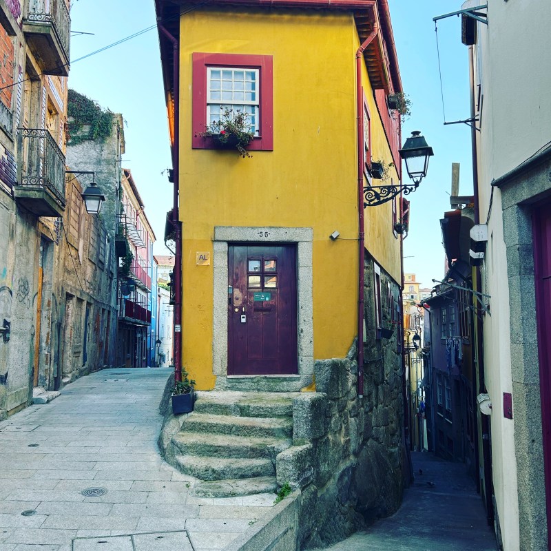 Narrow yellow house on a cobblestone street corner with stairs in an old town.