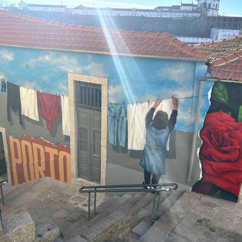 Street art mural of a person hanging laundry, with Porto text and a large red rose on a sunny day.