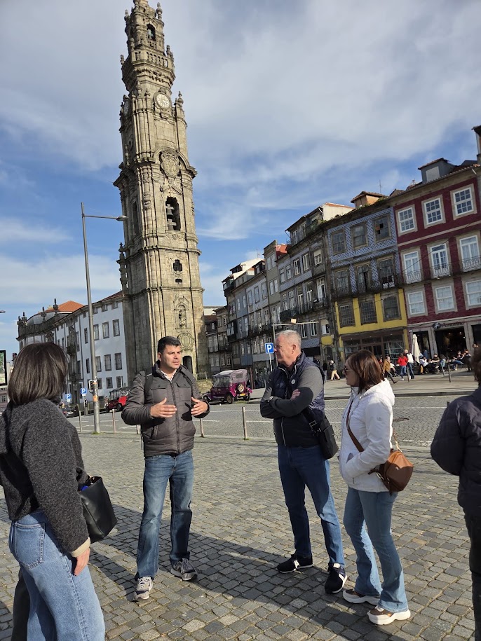 Group talking near a tall, historic clock tower in an urban setting.